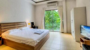Una habitación de hotel moderna con una cama grande, un televisor y vistas a la vegetación por la ventana.