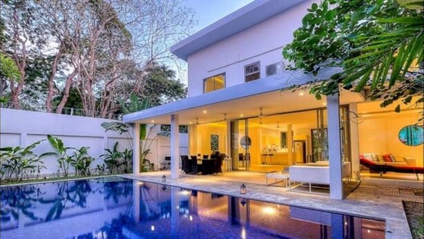 Una casa moderna con piscina, mobiliario de exterior y un patio cubierto.