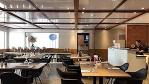 Ein modernes Restaurant mit hoher Decke, Glaswänden und einer Mischung aus Holz- und schwarzen Stühlen.