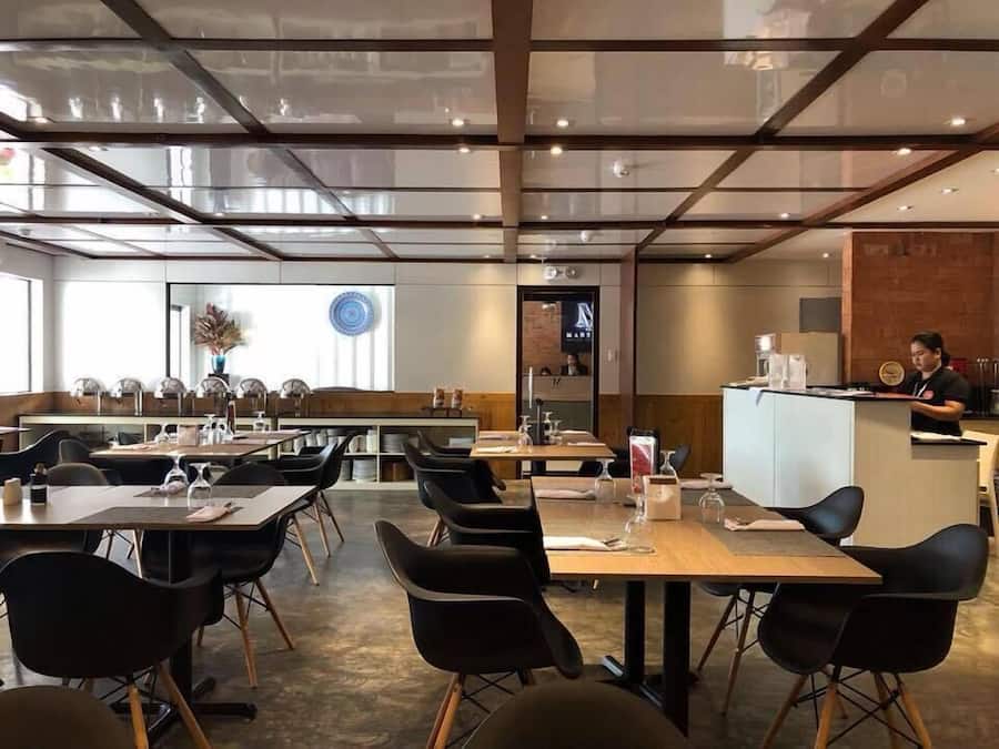 Een modern restaurant met een hoge plafond, glazen scheidingswanden en een combinatie van houten en zwarte stoelen.