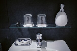 A bathroom with a glass shelf holding two glass tumblers and a white soap dispenser.