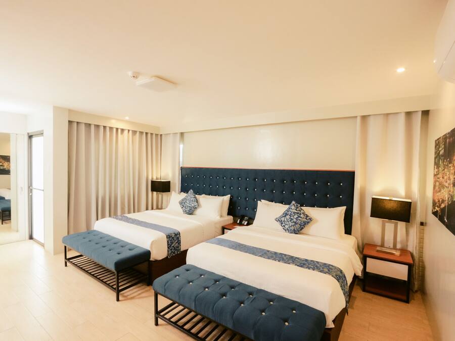 A hotel room with two beds, a bench, a nightstand, and a door leading to another room.