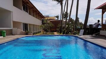 Une piscine à l’eau d’un bleu limpide, entourée de palmiers et bordée d’un bâtiment doté d’un balcon.