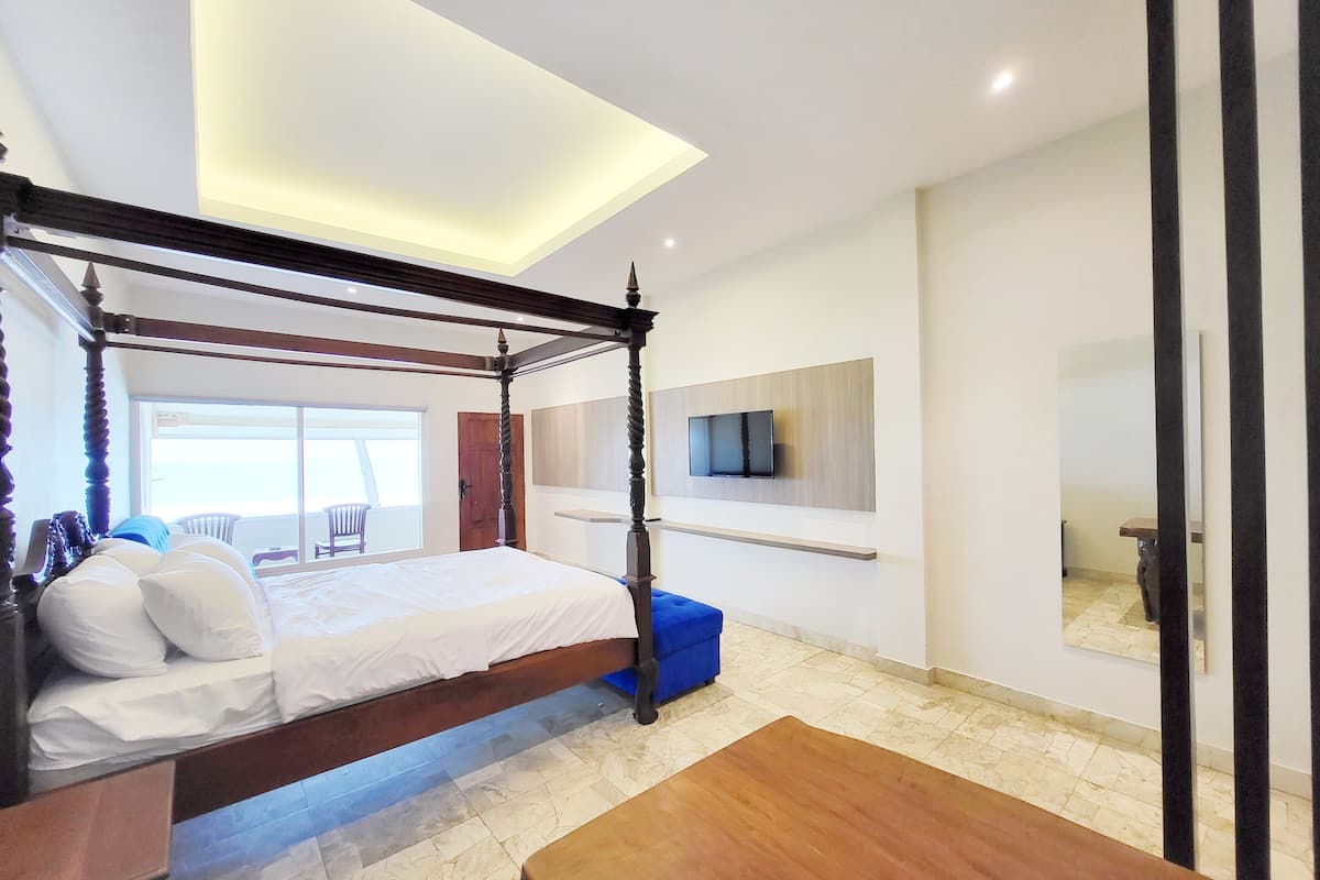 A modern bedroom with a four-poster bed, a mounted TV, and a balcony view.