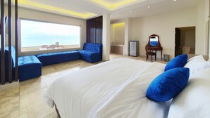 A modern hotel room with a large bed, a seating area by the window, and a view of the sea. - 77 Sunset Plaza (Cisolok)
