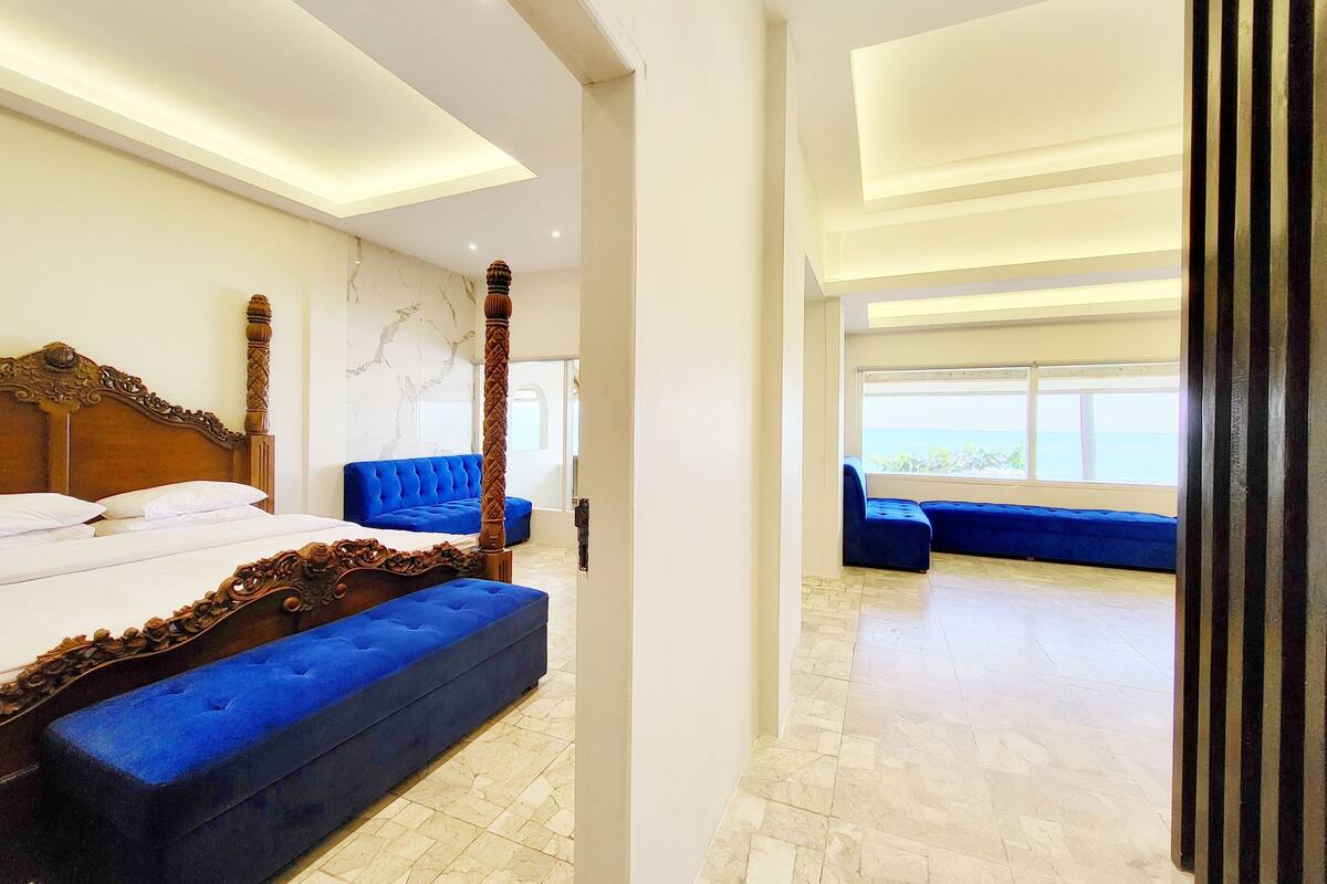 A modern hotel room with a large bed, a blue sofa, and a view of the sea.