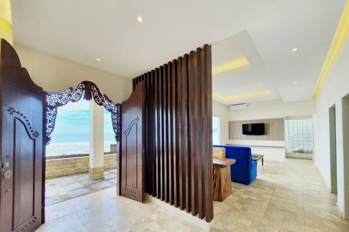 A modern hotel lobby with a large wooden door, a blue sofa, and a TV mounted on the wall.