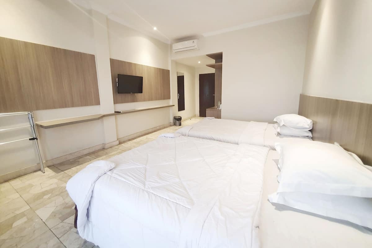 A hotel room with two beds, a TV mounted on the wall, and a trash bin.