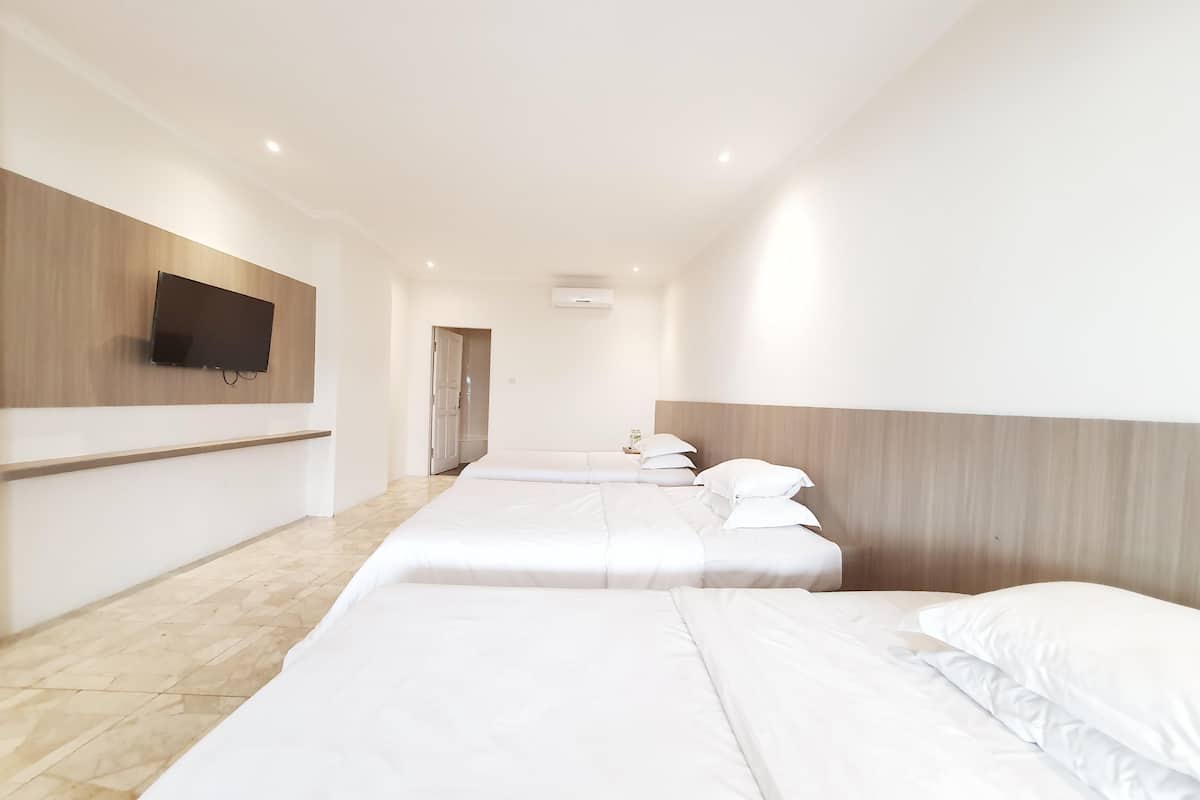 A hotel room with a long bed, a TV mounted on the wall, and a wooden headboard.