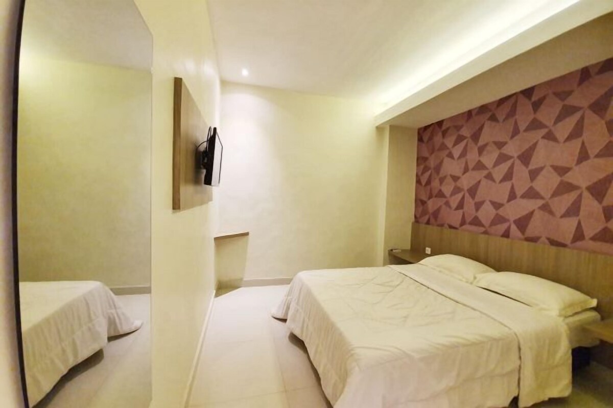 A hotel room with a large bed, a bedside table, and a wall-mounted TV.