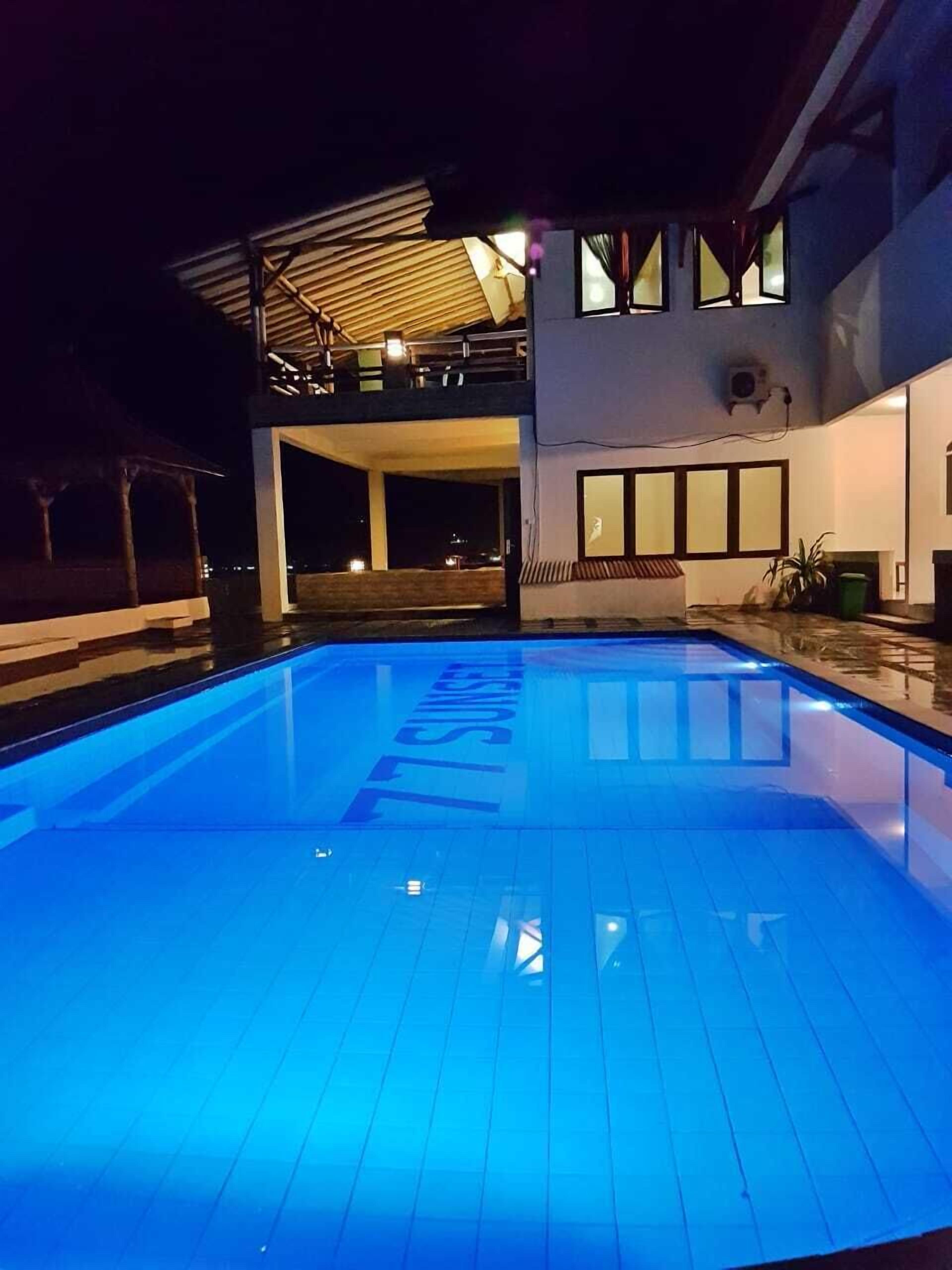 Una piscina de tonalidad azul, un espacio al aire libre cubierto y un edificio moderno con grandes ventanales.
