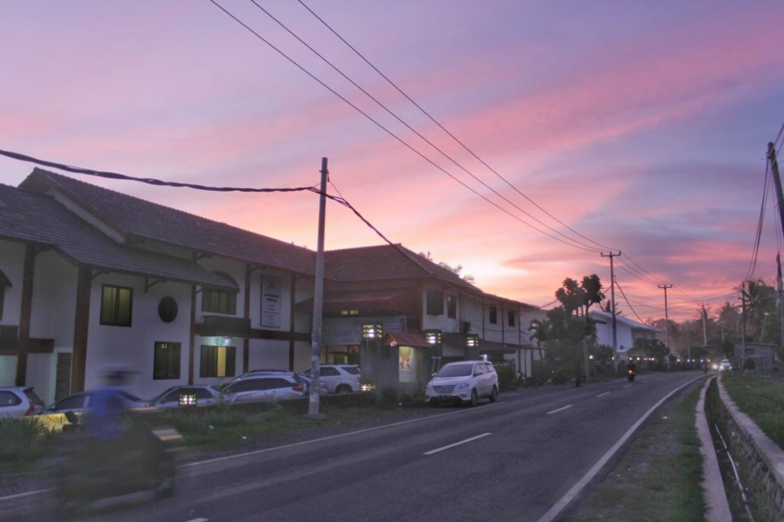Vista de la calle con edificios, coches aparcados y un cielo al atardecer.