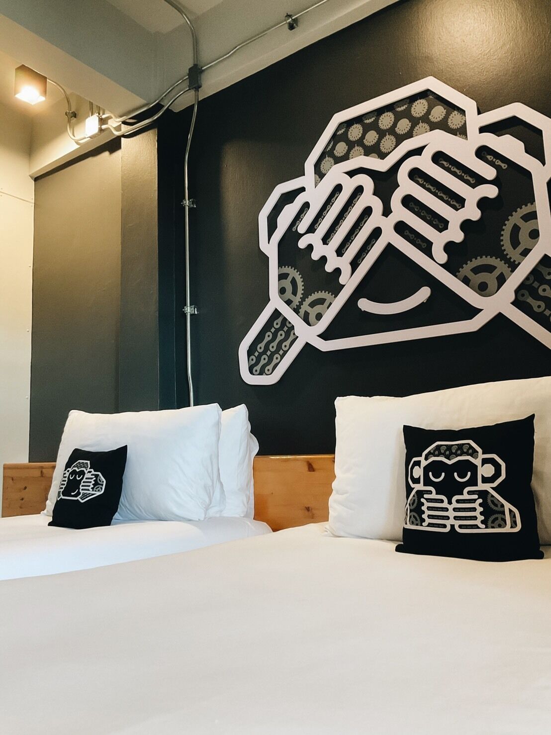 A hotel room with a bed, white pillows, and a large wall decoration of a hand holding a beer mug.
