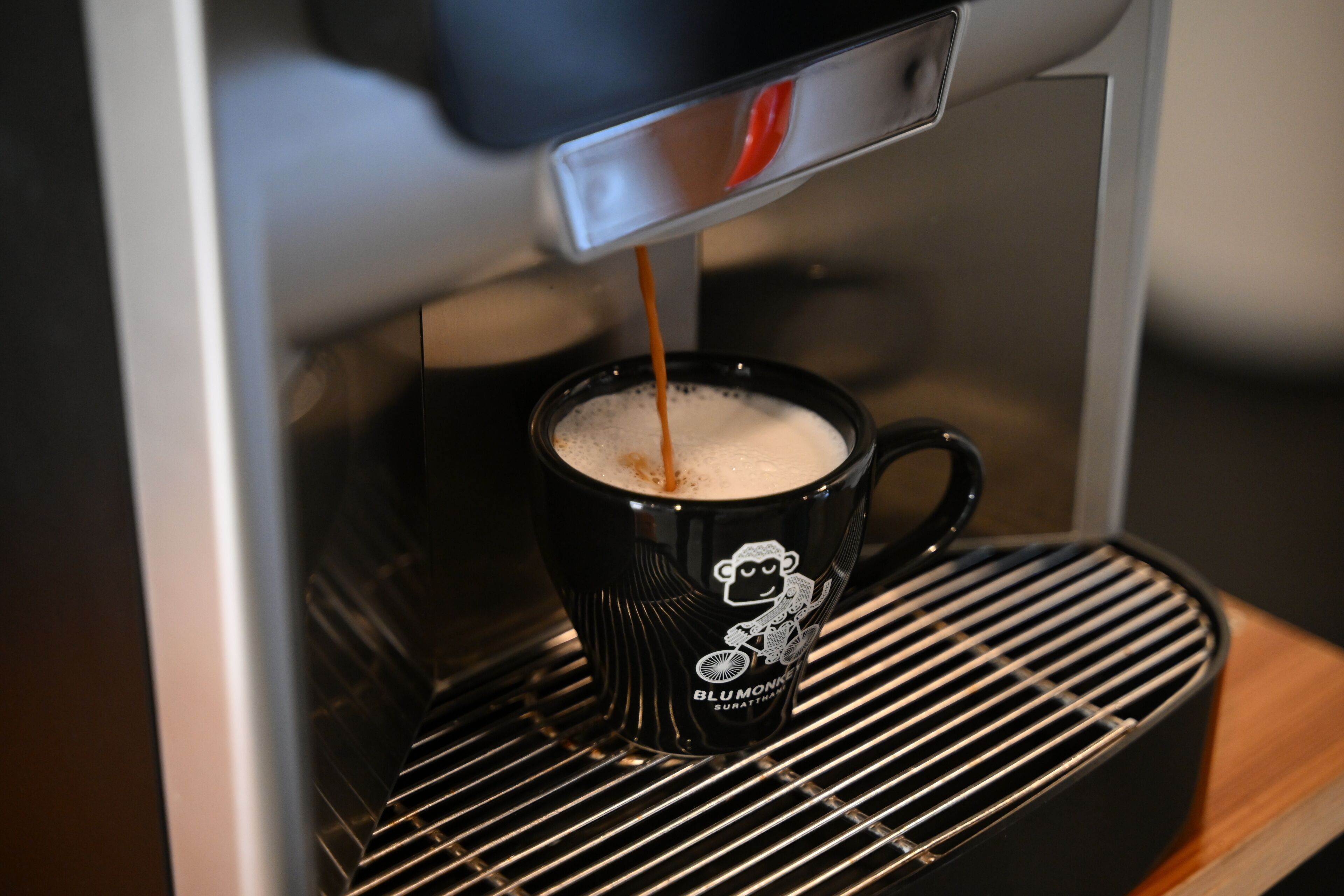 A coffee machine dispensing coffee into a black mug with a monkey design.