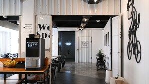 Een modern interieur met een digitale kiosk, een zithoek en bewegwijzering naar voorzieningen zoals ontbijt en de aapmarkt.