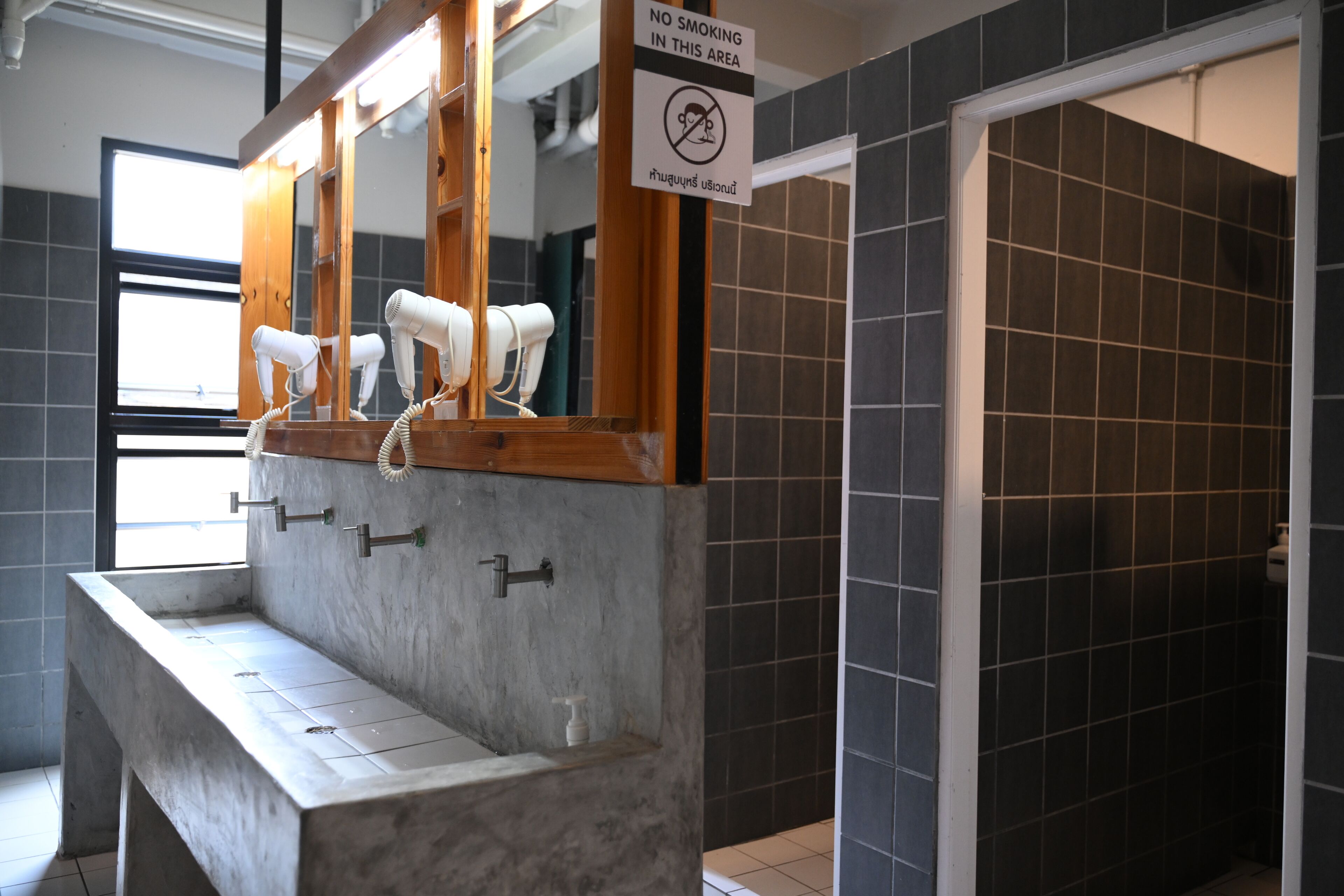 A bathroom with a no-smoking sign, a mirror, and hair dryers on a counter.