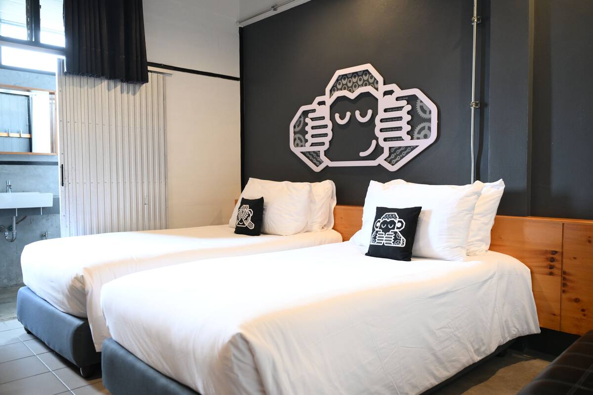 A hotel room with two beds, a large wall mural, a window with curtains, and a wooden headboard.