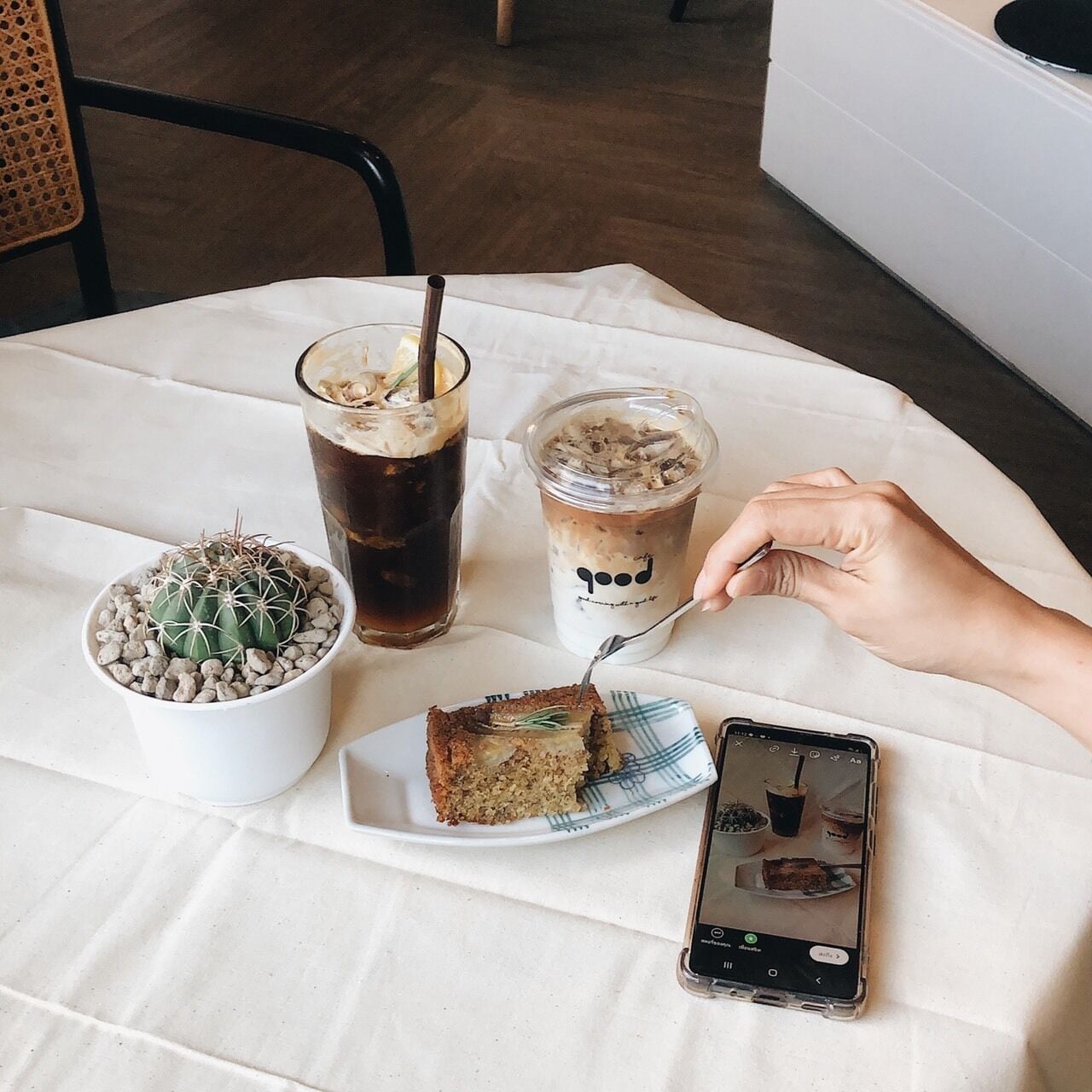 A table with a slice of cake, iced coffee, a jar of dessert, and a cactus plant.