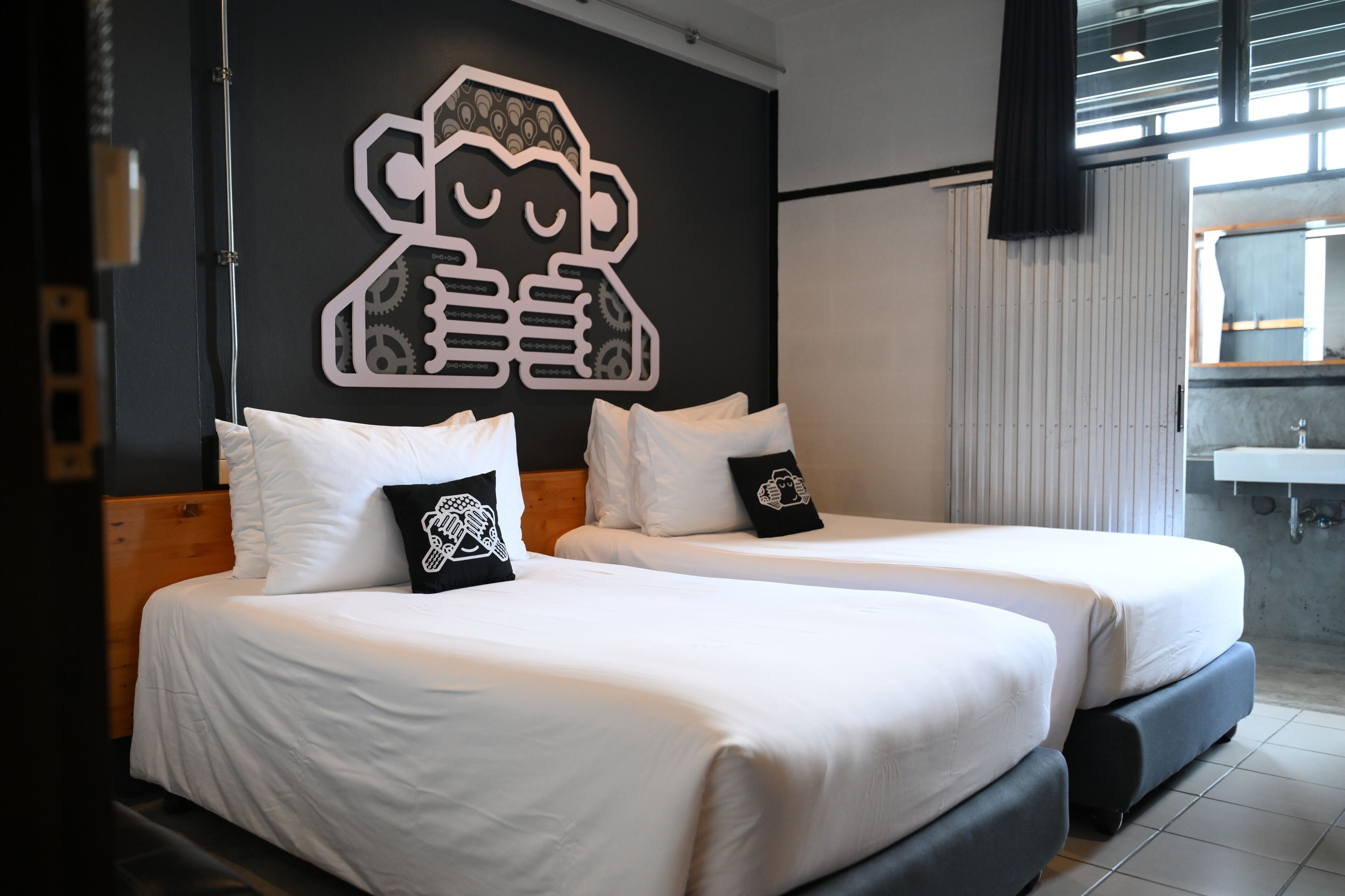 A hotel room with two beds, a large wall mural, a window, and a bathroom with a sink.
