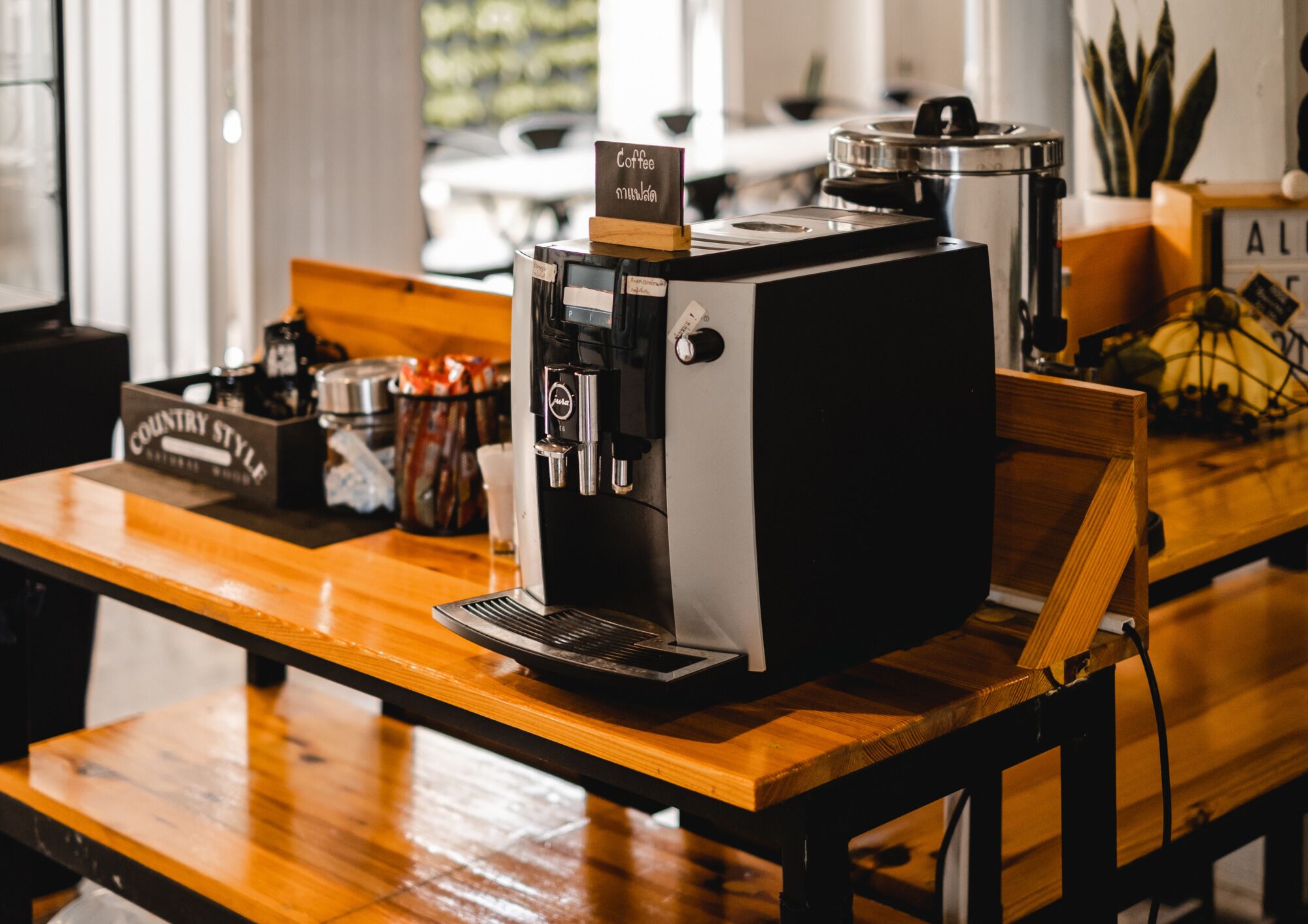 A coffee machine on a wooden table with a coffee bean container and a sign that reads "Coffee Country Style."