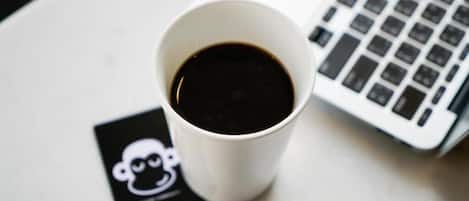 Una taza blanca de café sobre una mesa con una computadora portátil y una tarjeta negra con un diseño blanco.