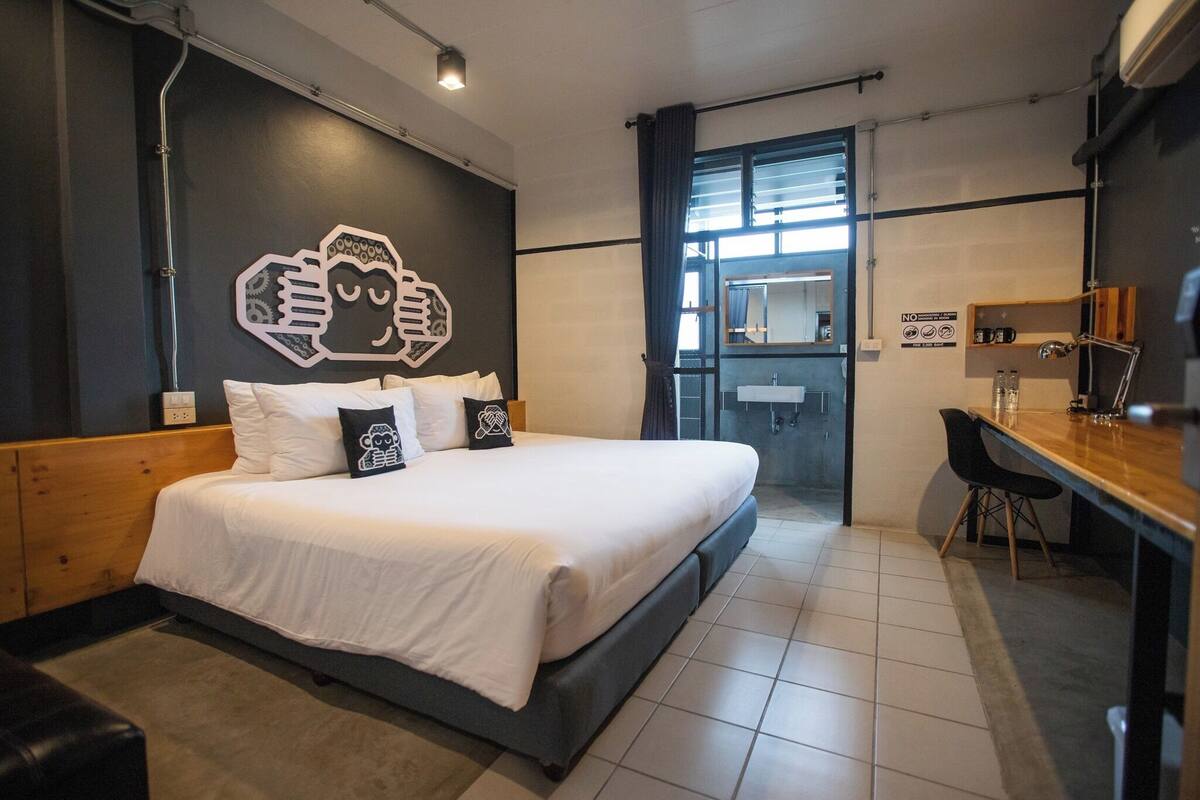 A modern hotel room with a large bed, a desk, and a bathroom visible through an open door.