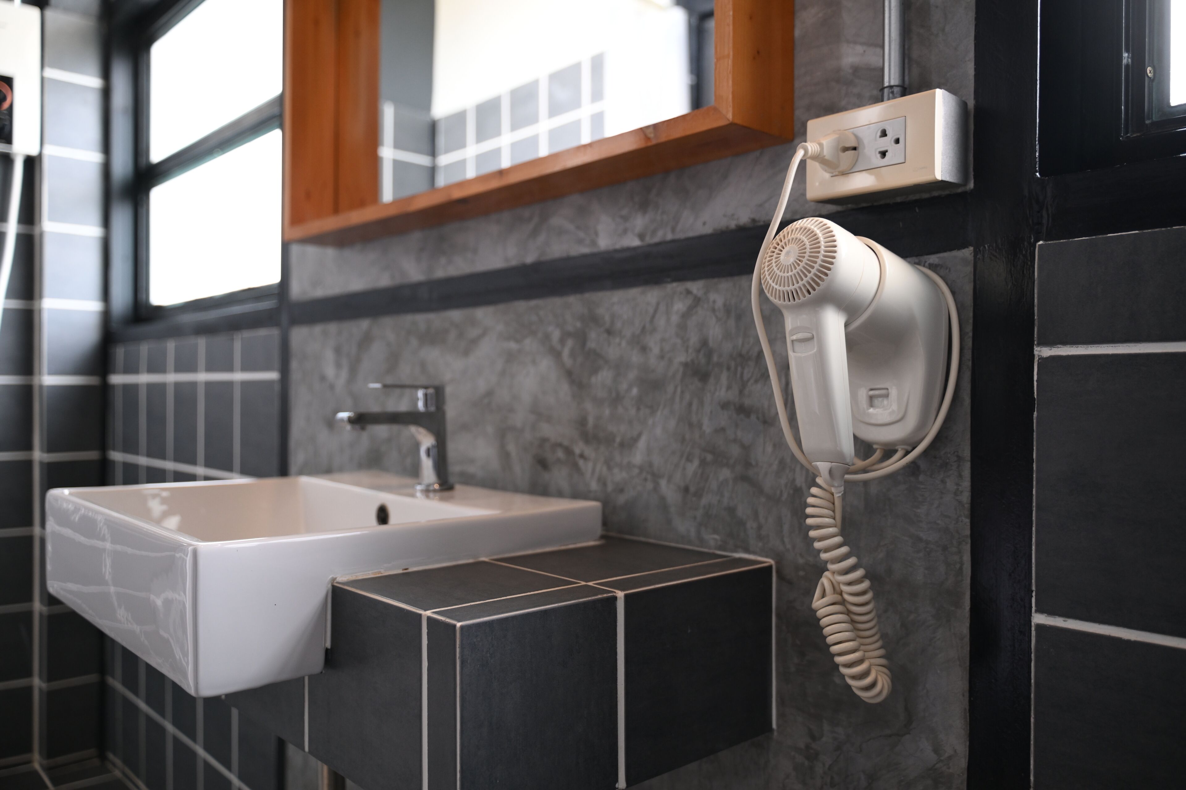 A bathroom with a white sink, a hairdryer, and a mirror above the sink.