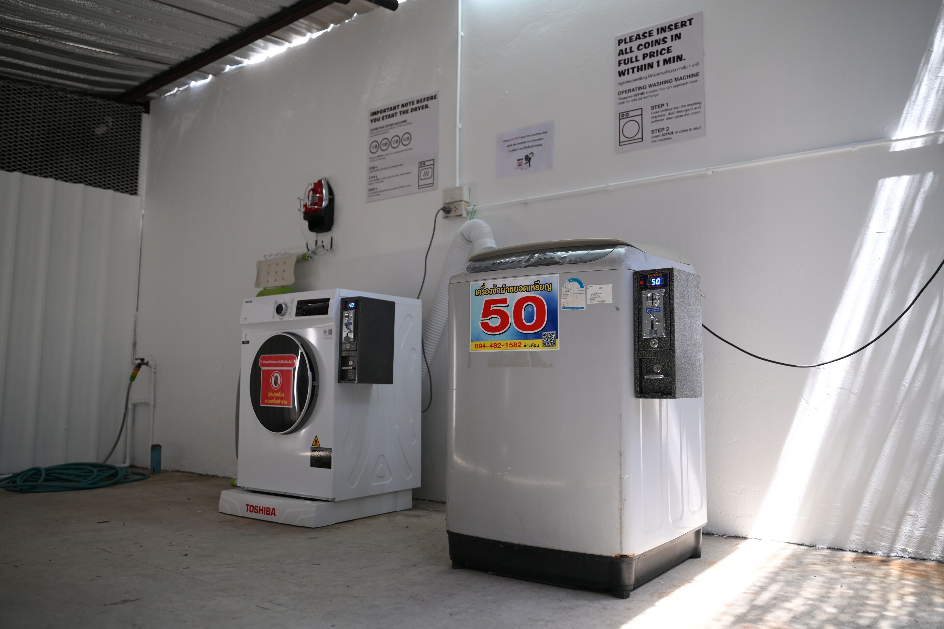 A washing machine and a dryer in a room with white walls, a metal ceiling, and a hose on the floor.