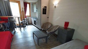 Een compacte hotelkamer met een bed, een klein tafeltje, een stoel en een kitchenette.