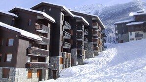 Een meerhoog hotel met balkons, een gevel van steen en hout, en een besneeuwde berg op de achtergrond.
