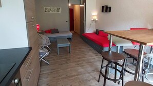 Een compacte kamer met een bed, een klein tafeltje en een stoel. Er is een deur die naar een andere kamer leidt.