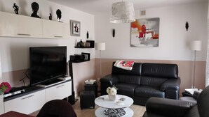 A modern living room with a flat-screen TV, black leather sofa, and a white coffee table.