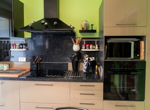 A modern kitchen with a black countertop, stainless steel appliances, and a green accent wall.