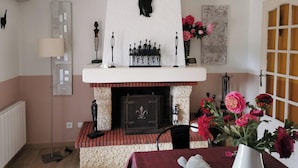A cozy living room with a fireplace, a table with a vase of flowers, and a decorative shelf with figurines.