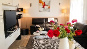 A modern living room with a flat-screen TV, leather sofa, and a coffee table with a vase of flowers.