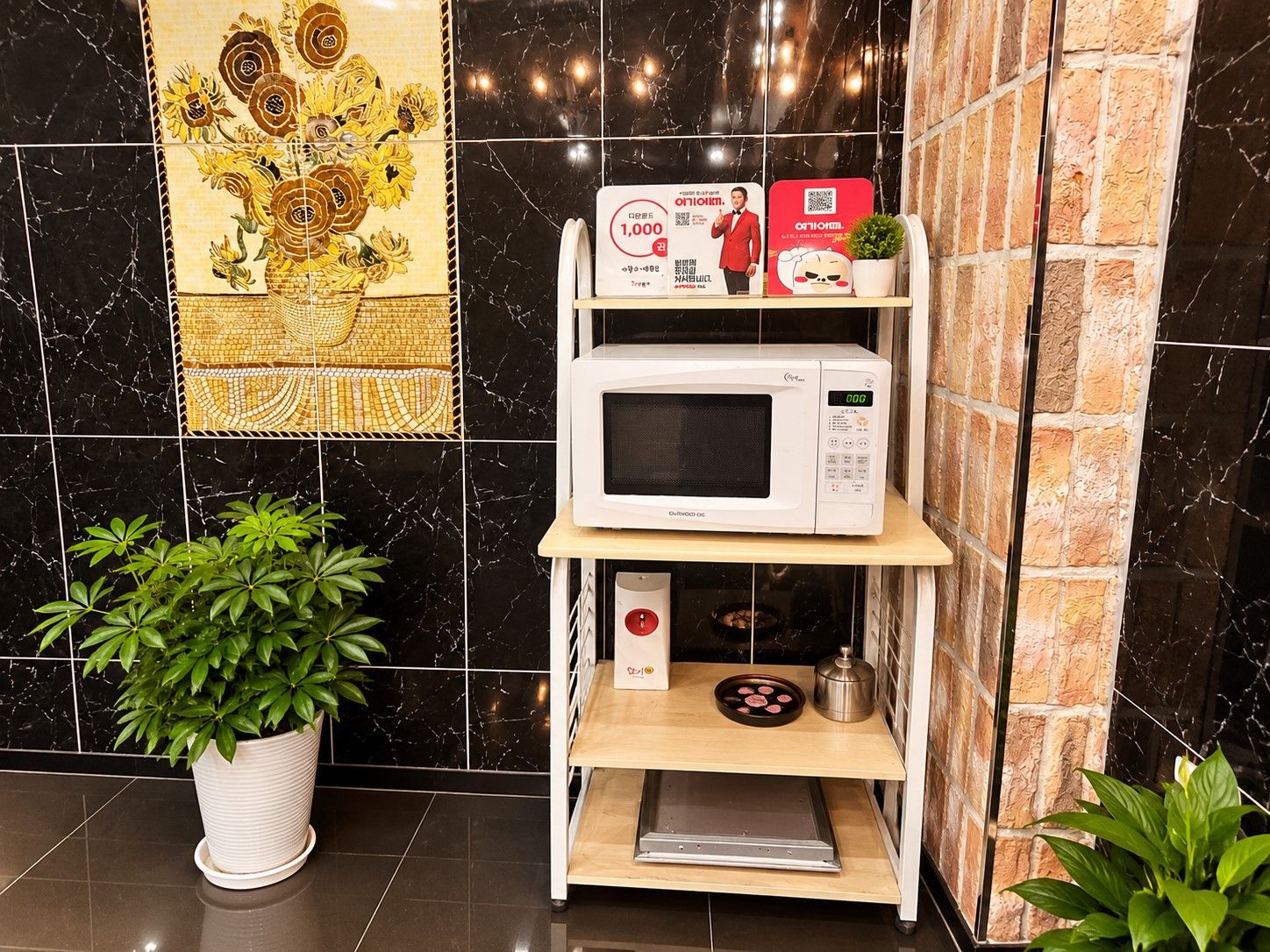 Un área de cocina con un microondas en un estante, una planta en maceta y un azulejo decorativo.