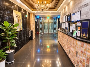 A hotel lobby with a reception desk, a chandelier, a plant, and a wall with a 'SWISS' sign. - Hotel Swiss  (Seoul)