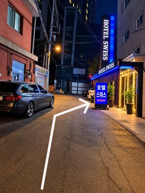 A nighttime street view with a hotel named 'HOTEL SWISS' and a sign indicating a direction to 'Hotel Swiss.' - Hotel Swiss  (Seoul)