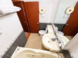 A bathroom with a toilet, sink, and bathtub. There are towels on a shelf and toilet paper dispensers on the wall. - Hotel Swiss  (Seoul)