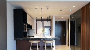 A modern kitchen with a marble countertop, two wooden bar stools, pendant lighting, and a view into the adjacent dining area. - Gallipoli Anggun Suites (Kuala Lumpur)