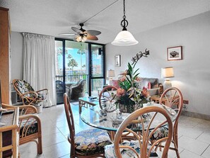 Relax in this open-plan living area with a glass-top coffee table and wicker chairs, surrounded by a stunning view of palm trees.