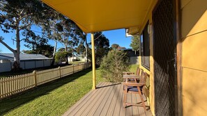 A wooden deck with a yellow awning, a wooden fence, and a small table and chair set. - Alwyns By The Sea holiday home (Inverloch)