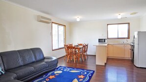 Ein kompakter Wohnbereich mit Sofa, Esstisch, Stühlen, einer Küchenzeile und einem gemusterten Teppich.