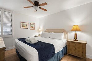 A hotel room with a bed, a nightstand, a lamp, a ceiling fan, and two framed pictures on the wall.