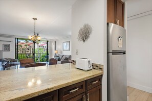 A kitchen with a stainless steel refrigerator, a toaster, and a dining area with a table and chairs. - 1 Bedroom w/Modern Kitchen - Kamaole Sands 6206 (KIHEI)