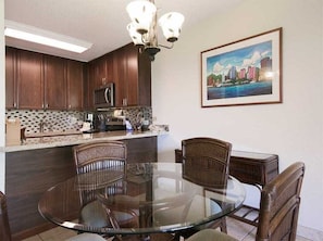 Une cuisine moderne avec des meubles de couleur sombre en bois, une table à manger en verre et un tableau représentant un paysage urbain accroché au mur.