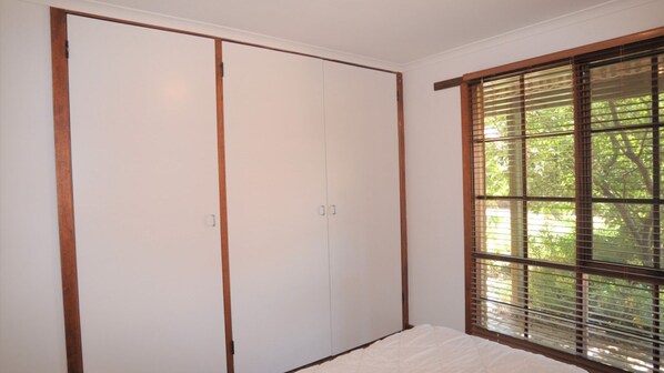A bedroom with a large wardrobe, a window with blinds, and a bed.