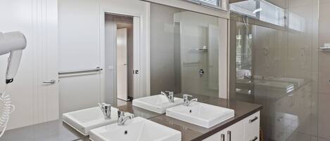 Ein modernes Badezimmer mit zwei Waschbecken, einem Föhn und einer Duschkabine aus Glas.