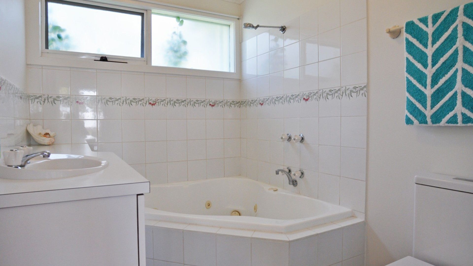 Un bany amb un lavabo blanc, una banyera i una finestra sobre el lavabo.