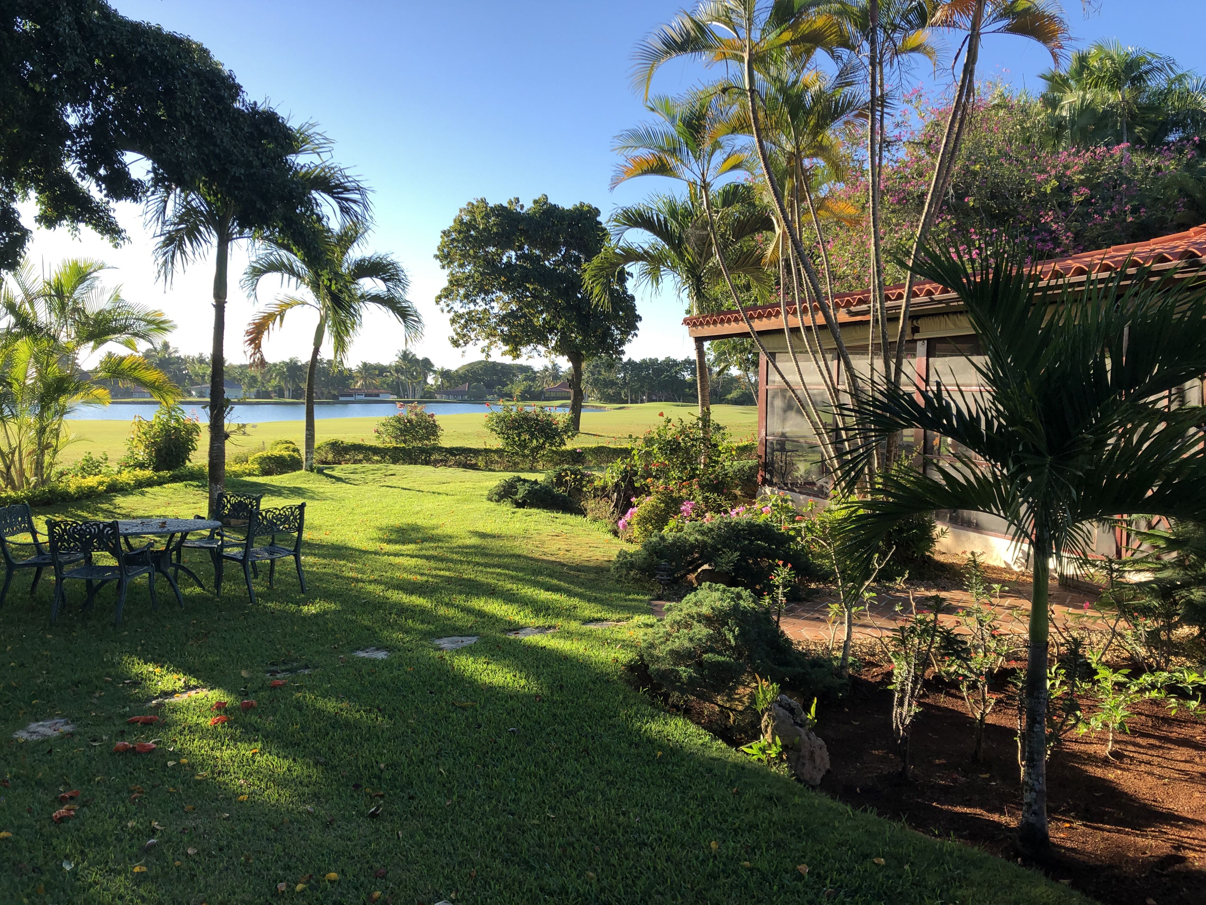 Un jardin bien entretenu avec une table et des chaises, un petit bâtiment avec un toit rouge et une vue sur un lac.